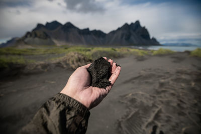 Midsection of person hand on rock at beach against sky