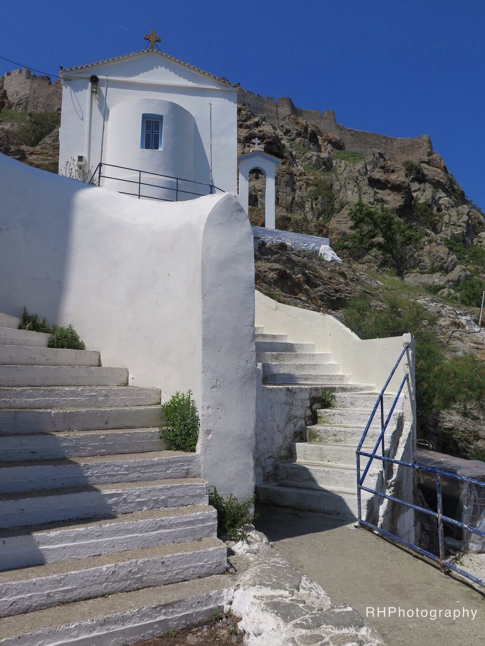 built structure, architecture, steps, building exterior, railing, clear sky, mountain, staircase, steps and staircases, sunlight, blue, sky, water, day, house, stairs, outdoors, nature, no people, low angle view