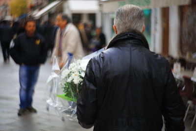 Rear view of man holding bouquet while walking in city