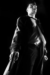 Man holding gun while standing against black background