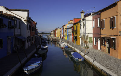 Boats moored in canal amidst buildings in city against sky