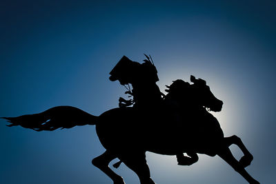 Low angle view of silhouette statue against clear blue sky