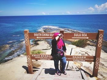 Woman standing against signboard on sunny day