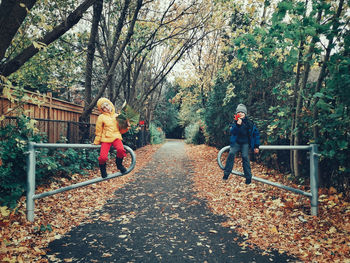 Siblings sitting on railings in park during autumn