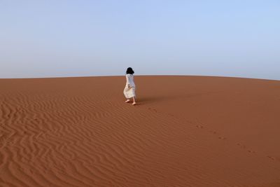 Girl walking on desert against sky