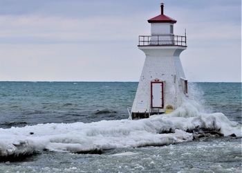 Lighthouse by sea against sky in winter 