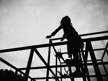 Low angle view of silhouette girl standing on jungle gym against sky