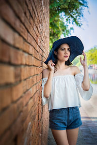 Woman wearing hat while standing by brick wall