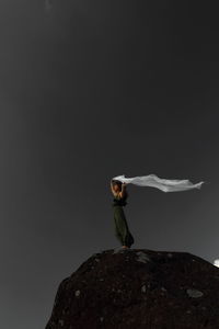Woman holding scarf while standing on rock formation against sky