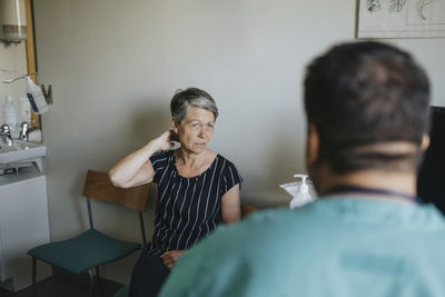 Senior woman touching neck while discussing with doctor in clinic