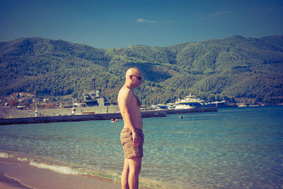 Shirtless man standing at beach against clear sky