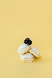 Delicious lemon iced cookies stacked with a blackberry on top on yellow backdrop