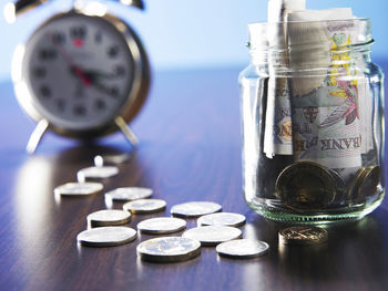 Close-up of currencies in jar with clock on table
