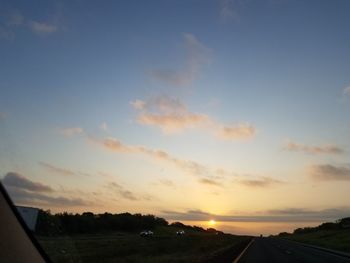 Road amidst field against sky during sunset