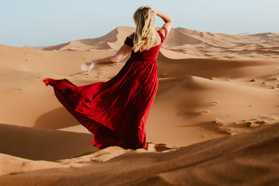 Young woman wearing red dress while standing at desert against clear sky