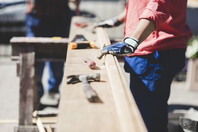 Midsection of senior woman standing by wooden plank in yard during sunny day