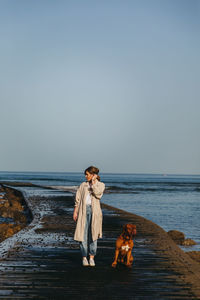 Woman with dog on beach against sky