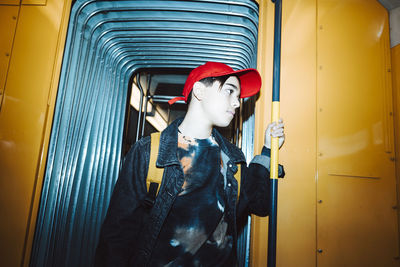 Contemplative boy wearing cap standing at doorway of tram