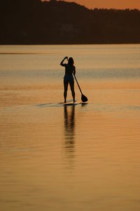 Silhouette man standing in sea against sky during sunset