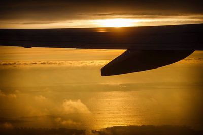 Silhouette airplane wing over sea against sky during sunset