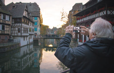 Mature man photographing buildings and canal in city