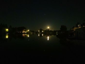 Illuminated buildings by river against sky at night