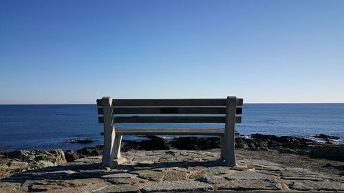 Bench on beach against clear blue sky