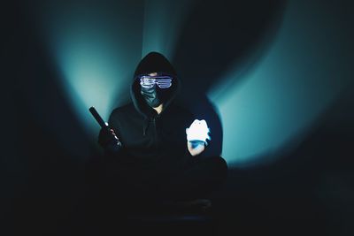 Man holding illuminated lights while sitting in darkroom