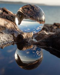 Close-up of crystal ball on sea shore against sky