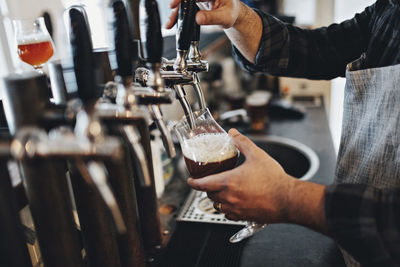 Midsection of bartender filling glass while using beer tap at restaurant