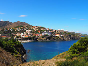 Aerial view of townscape by sea against blue sky