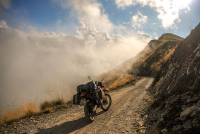 Motorcycle on dirt road on mountain against sky