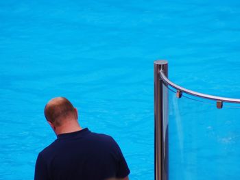 Rear view of man standing by swimming pool against sea