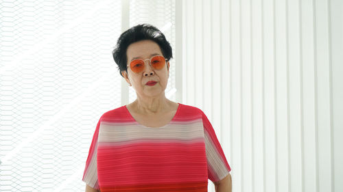 Portrait of woman wearing sunglasses standing against wall