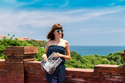 Woman wearing sunglasses standing by sea against sky