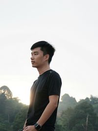 Side view of young man looking away against sky