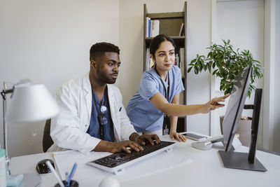 Doctor discussing with male coworker working on computer at desk in clinic