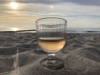 Glass of water on beach against sky during sunset