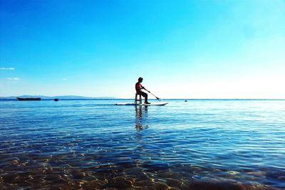 Man paddleboarding in sea against blue sky