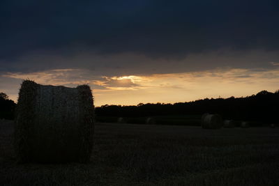 Hay bales on field against sky during sunset