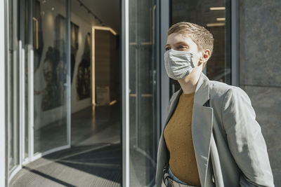 Mid adult woman wearing protective face mask standing in front of entrance
