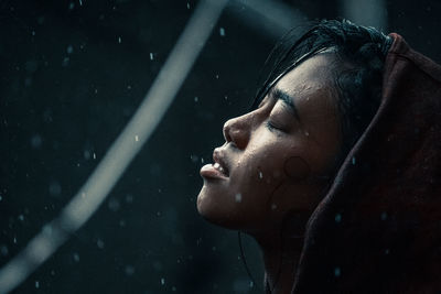 Close-up portrait of young woman with eyes closed in the blue rain
