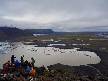 People on rock by lake against sky