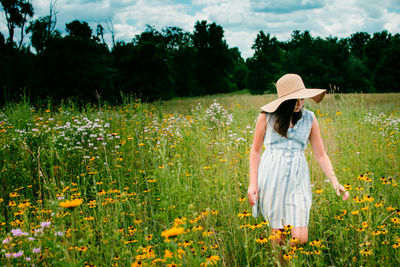 Rear view of woman standing by flowers on field