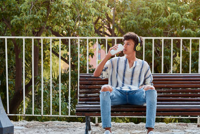 Young boy with afro hair drinks coffee while he is sitting on a bench