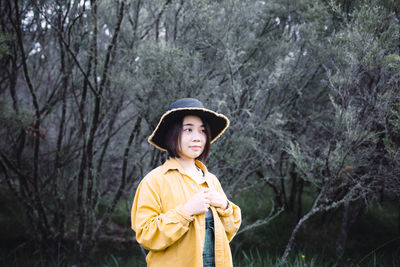 Woman wearing hat standing against trees in forest