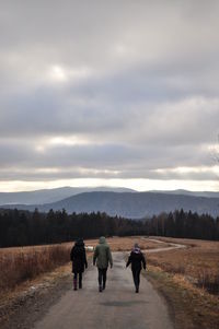 Rear view of people walking on road against cloudy sky