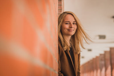Portrait of young woman with blond hair standing by column