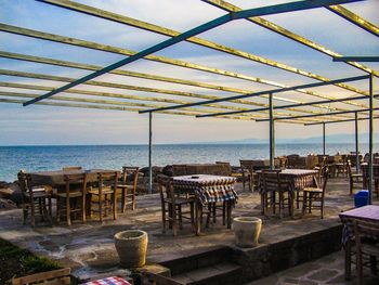 Tables and chairs in cafe by sea against sky