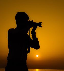 Silhouette man photographing by sea against sky during sunset